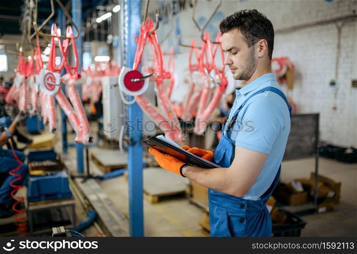 Bicycle factory, man with notebook checks bike assembly line. Male mechanic in uniform installs cycle parts in workshop, industrial manufacturing. Bicycle factory, man checks bike assembly line