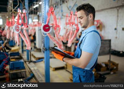 Bicycle factory, man with notebook checks bike assembly line. Male mechanic in uniform installs cycle parts in workshop, industrial manufacturing. Bicycle factory, man checks bike assembly line