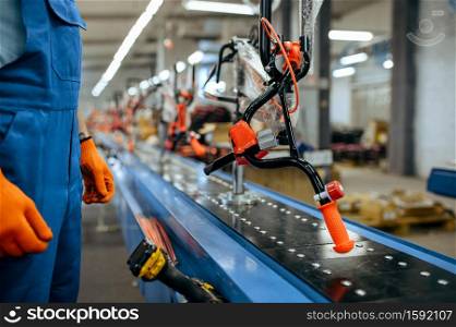 Bicycle factory, worker checks bike assembly line. Male mechanic in uniform installs cycle parts in workshop, industrial manufacturing. Bicycle factory, worker checks bike assembly line