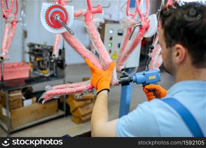 Bicycle factory, worker holds pink kid&rsquo;s bike. Male mechanic in uniform installs cycle parts, assembly line in workshop, industrial manufacturing. Bicycle factory, worker holds pink kid&rsquo;s bike