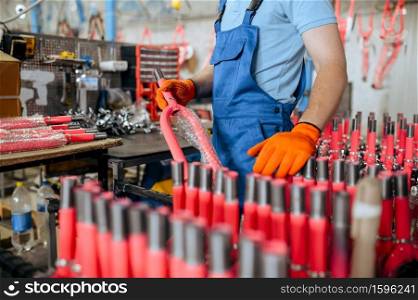 Bicycle factory, worker holds pink kid&rsquo;s bike fork. Male mechanic in uniform installs cycle parts, assembly line in workshop, industrial manufacturing. Bicycle factory, worker holds pink kid&rsquo;s bike fork