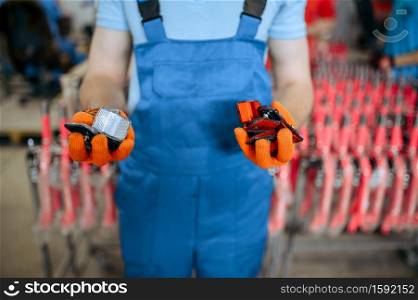 Bicycle factory, worker shows bike reflectors. Male mechanic in uniform installs cycle parts, assembly line in workshop, industrial manufacturing. Bicycle factory, worker shows bike reflectors