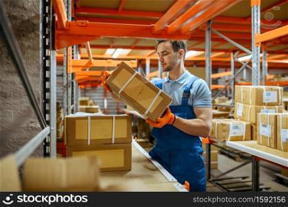 Bicycle factory, worker takes the box from the shelf in bikes warehouse. Male mechanic in uniform at the packs with cycle parts, assembly line in workshop, industrial manufacturing. Bicycle factory, worker takes box from the shelf