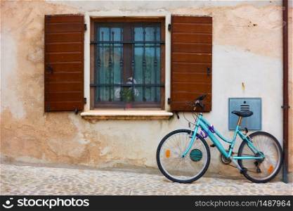 Bicycle in the street near wall of old house with window with open shurrers in a small italian town in Emilia-Romagna, Italy