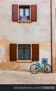 Bicycle in the street near wall of old house with window with open shurrers, Italy -- Italian urban view