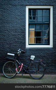 Bicycle parked at house wall in Amsterdam street. Bicycle is a famous very popular means of transport in Netherlands. Amsterdam, Netherlands. Bicycle near wall of old house in Amsterdam street