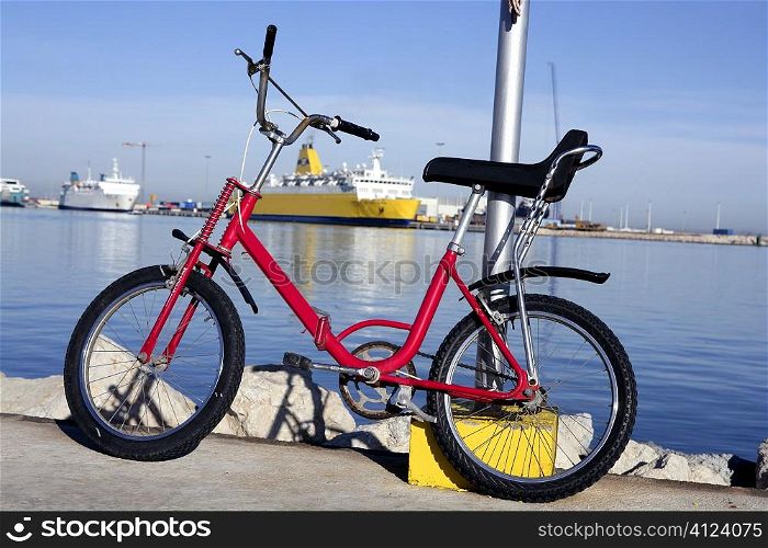 bicycle parked in a harbour over blue water, yellow boat, red bike