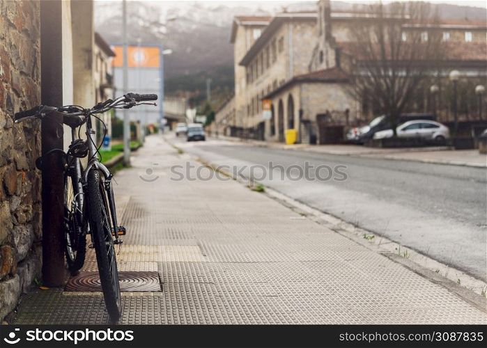 Bicycle parked on sidewalk near city street in Spain. Bike lean on pole beside old building. Front view of bicycle on blurred building, car driving on the road, and mountain background. Europe travel.