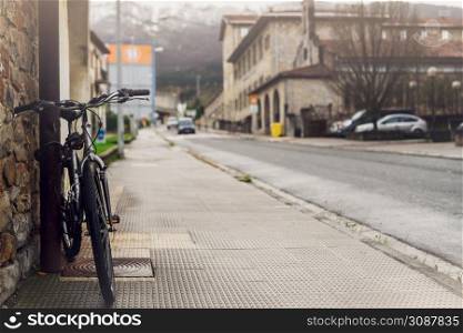 Bicycle parked on sidewalk near city street in Spain. Bike lean on pole beside old building. Front view of bicycle on blurred building, car driving on the road, and mountain background. Europe travel.