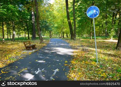 Bicycle path and a footpath with warning sign in autumn park.