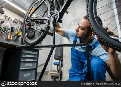 Bicycle repair in workshop, man checks the wheel for backlash. Mechanic in uniform fix problems with cycle, professional bike repairing service. Bicycle repair, man checks the wheel for backlash