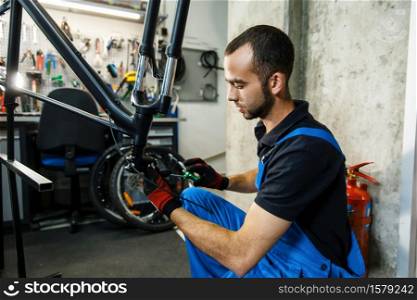 Bicycle repair in workshop, man fixing crank. Mechanic in uniform fix problems with cycle, professional bike repairing service. Bicycle repair in workshop, man fixing crank