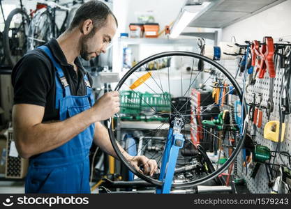 Bicycle repair in workshop, man works with wheel. Mechanic in uniform fix problems with cycle, professional bike repairing service. Bicycle repair in workshop, man works with wheel