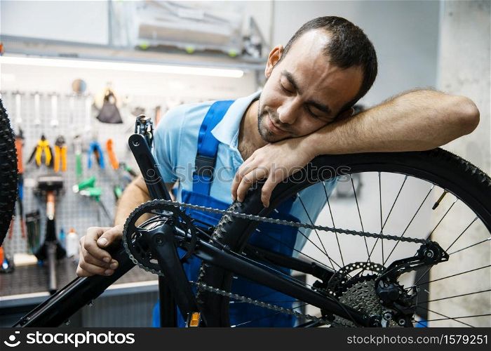 Bicycle repair in workshop, tired repairman sleeps at workplace. Mechanic in uniform fix problems with cycle, professional bike repairing service. Bike repair, tired repairman sleeps at workplace