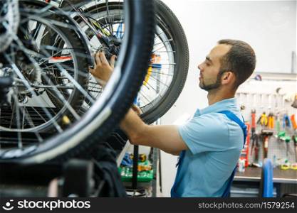 Bicycle workshop, man finished assembling. Mechanic in uniform fix problems with cycle, professional bike repairing service. Bicycle workshop, man finished assembling