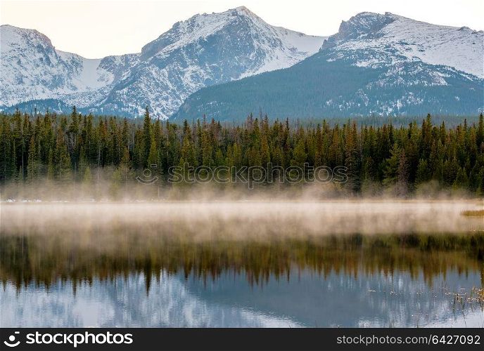 Bierstadt Lake and reflection with mountains in snow around at autumn. Fog on the water. Rocky Mountain National Park in Colorado, USA.