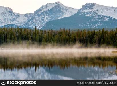 Bierstadt Lake and reflection with mountains in snow around at autumn. Fog on the water. Rocky Mountain National Park in Colorado, USA.