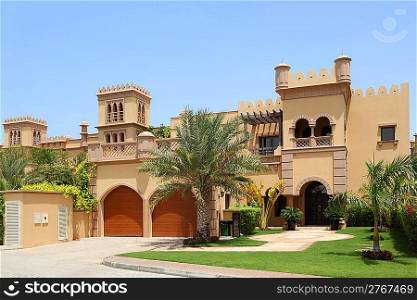 big arabian style house with two garages and archs, yard with palms
