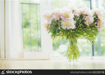 Big beautiful pale pink peonies bouquet in glass vase over window background. Light Home decoration with flowers and vase. Living room interior