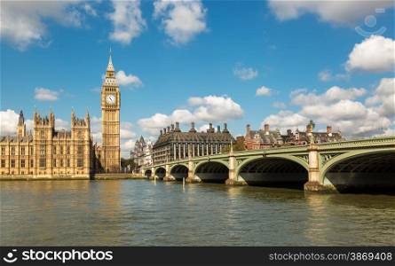 Big Ben and the Houses of Parliament in London with Westminster Bridge and the River Thames in the foreground against a blue sky with fluffy white clouds