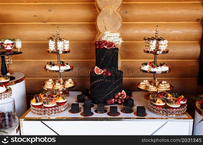 big black birthday cake with fresh fruits and sweets on a festive table. Candy bar. Table with different sweets for party.. big black birthday cake with fresh fruits and sweets on a festive table. Candy bar. Table with different sweets for party