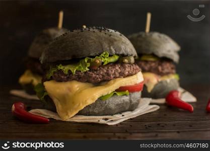 Big Black burger. Black burger with beef meat cheese lettuce onion, tomato and sauce served on black wooden table