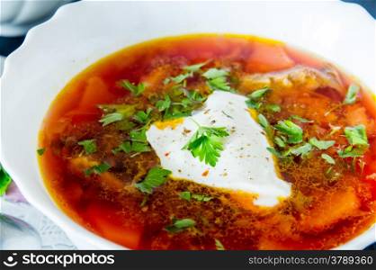 big bowl of borscht with sour cream and herbs on black table