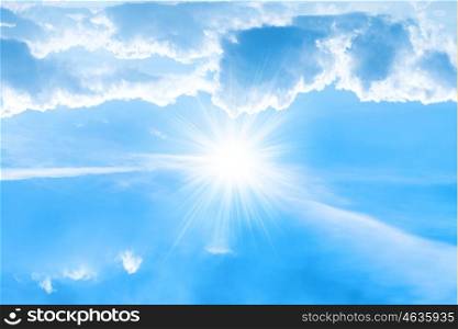 Big bright sun with sunrays on white clouds and blue sky