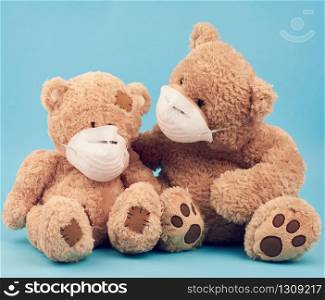 big brown teddy bears are sitting in medical masks on a blue background, concept of protection from respiratory disease, virus and individual respiratory protection