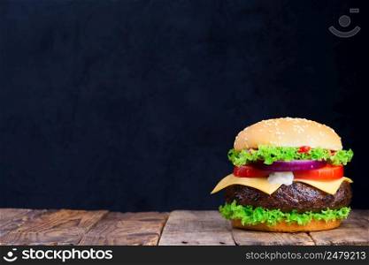 Big burger on wooden table with blank black chalkboard on background with copy space