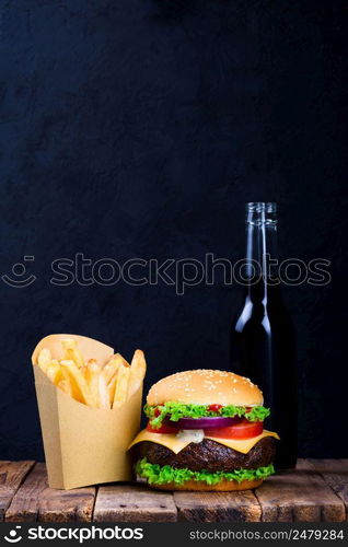 Big burger with french fries and drink on wooden table with dark stone background with copy space