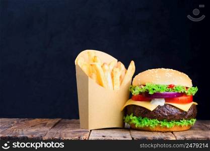Big burger with french fries on wooden table with blank black chalkboard on background with copy space