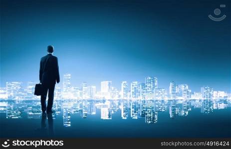 Big city life. Businessman standing with back against night city panoramic view