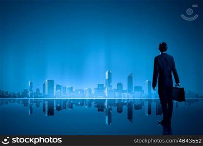 Big city never sleeps. Businessman standing with back against night city panoramic view