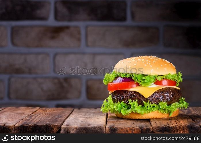 Big classic hamburger on wooden table and brick wall on background with copy space