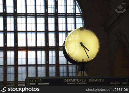 Big clock inside a train station on top of the time table