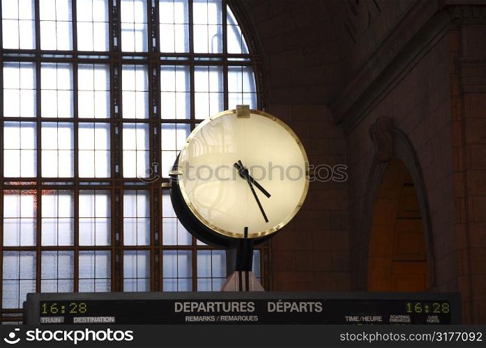 Big clock inside a train station on top of the time table