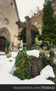 Big cross covered by snow on ancient graveyard at church