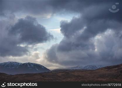 Big dramatic stormy skies landscape image over snowcapped mountains in Scottish Highlands