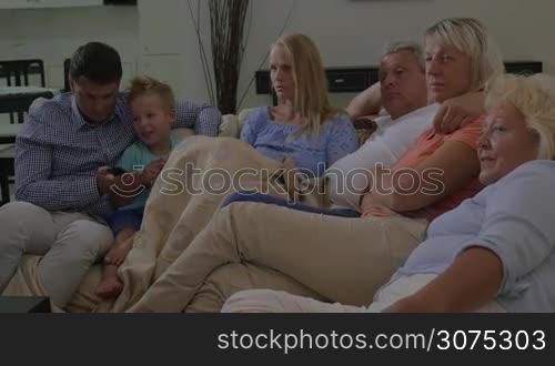 Big family relaxing at home. Parents, child and grandparents watching TV. Father and son changing channels with remote