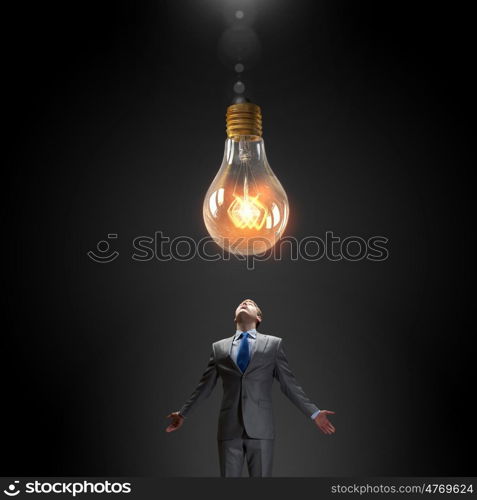 Big idea. Young businessman looking up at glass glowing light bulb