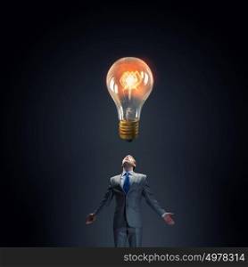 Big idea. Young businessman looking up at glass glowing light bulb