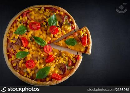 Big italian pizza with tomatoes and basil on a black background. Big pizza with cherry tomatoes, cheese and green basil on a black background. National Italian dish of Mediterranean cuisine. Top view, place for text.. Big italian pizza with tomatoes and basil on a black background.