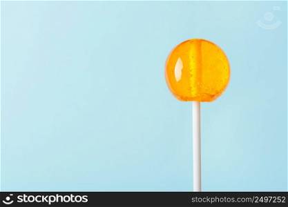 Big orange lollipop on blue pastel background