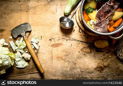 big pot of soup with beef and fresh vegetables. On wooden background.. big pot of soup with beef and fresh vegetables.