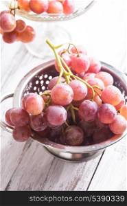 Big red grapes in colander on the wood background