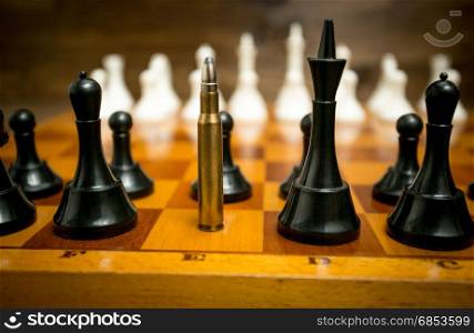 Big riffle bullet in row of black chess pieces. Concept of gun power