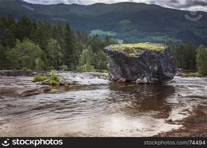 big rock in a river in norway with background of mountains and green forest. big rock in river in norway