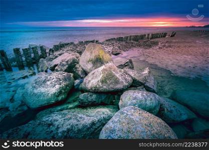 Big rocky stones in dutch lake at twilight in the early morning. Long breakwater at cloudy sunset