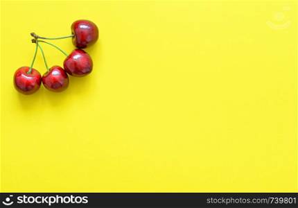 Big sweet cherry isolated on bright yellow background. Summer background. Flat lay, top view. Four red cherries.. Big sweet cherry isolated on bright yellow background.